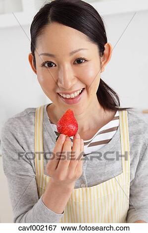 Stock Photo - Woman eating strawberry in an open kitchen. Fotosearch