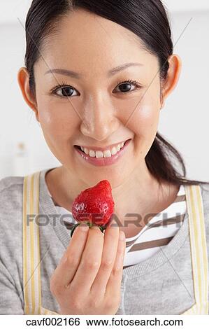 Stock Photograph - Woman eating strawberry in an open kitchen. Fotosearch