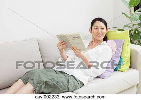 Stock Image - Woman reading a book on the sofa. Fotosearch