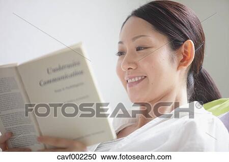 Stock Image - Woman reading a book on the sofa. Fotosearch