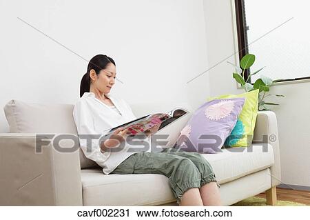 Stock Image - Woman reading a magazine on the sofa. Fotosearch