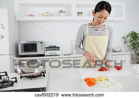 Stock Photo - Woman slicing vegetables in an open kitchen. Fotosearch