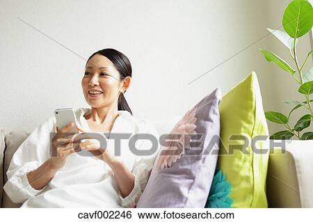 Woman using a Smartphone on the sofa View Large Photo Image Stock Photograph - Woman using a Smartphone on the sofa. Fotosearch