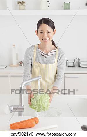 Stock Image - Woman washing cabbage in an open kitchen. Fotosearch