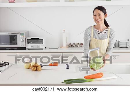 Stock Image - Woman washing cabbage in an open kitchen. Fotosearch