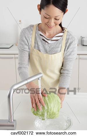 Stock Image - Woman washing cabbage in an open kitchen. Fotosearch