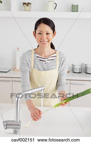 Stock Image - Woman washing green onions in an open kitchen. Fotosearch