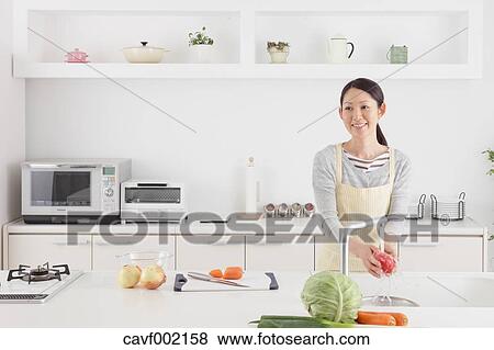 Stock Photo - Woman washing tomatoes in an open kitchen. Fotosearch