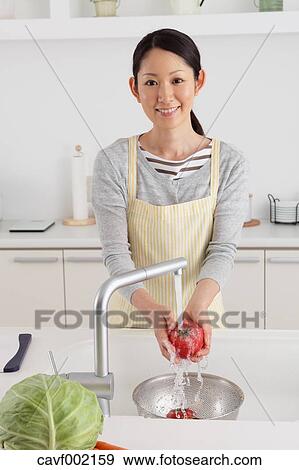 Stock Photo - Woman washing tomatoes in an open kitchen. Fotosearch