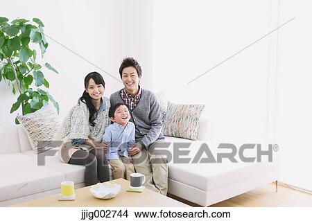 Picture - Young adult couple and their son on the sofa smiling at camera. Fotosearch