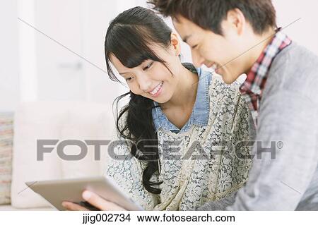 Young adult couple relaxing with tablet on the sofa View Large Photo Image Picture - Young adult couple relaxing with tablet on the sofa. Fotosearch