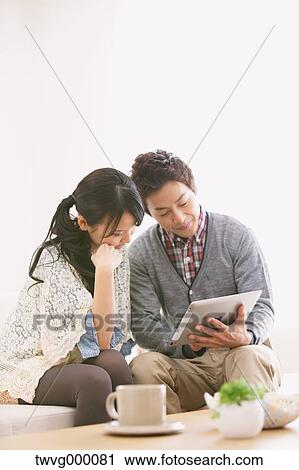 Stock Image - Young adult couple relaxing with tablet on the sofa. Fotosearch