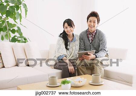 Stock Photo - Young adult couple relaxing with tablet on the sofa. Fotosearch