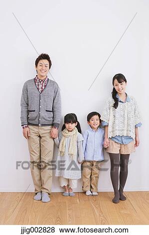 Stock Photo - Young adult couple with their kids standing in front of a white wall. Fotosearch