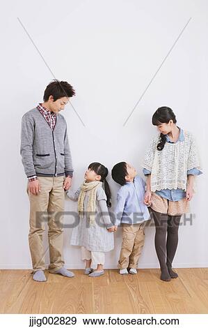 Stock Photo - Young adult couple with their kids standing in front of a white wall. Fotosearch