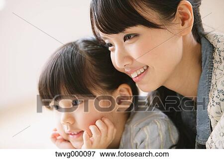 Stock Photo - Young adult mother and daughter smiling while looking away. Fotosearch