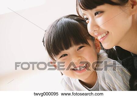 Stock Photography - Young adult mother and daughter smiling while looking away. Fotosearch