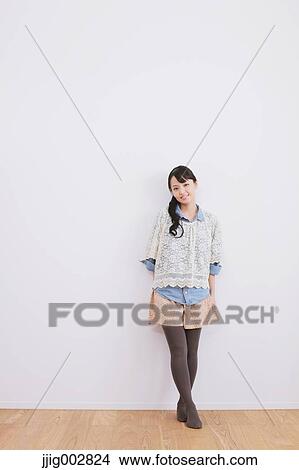 Young adult woman leaning against a white wall and smiling at camera View Large Photo Image Picture - Young adult woman leaning against a white wall and smiling at camera. Fotosearch