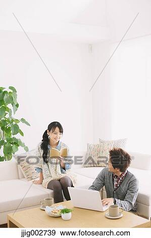 Young couple using computer and reading a book while relaxing on the sofa View Large Photo Image Stock Photo - Young couple using computer and reading a book while relaxing on the sofa. Fotosearch