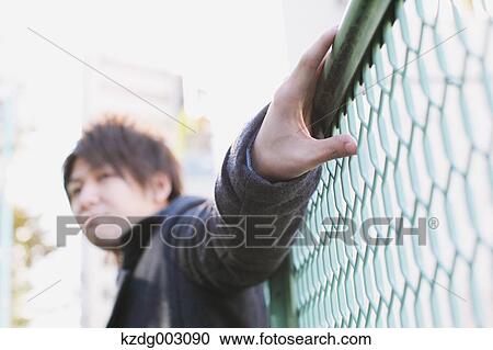 Young man leaning on a fence View Large Photo Image Stock Image - Young man leaning on a fence. Fotosearch
