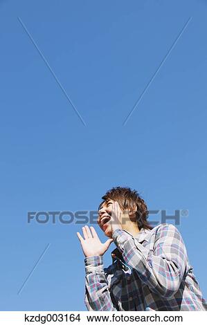Picture - Young man shouting against blue sky. Fotosearch