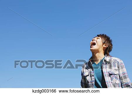 Stock Photograph - Young man shouting against blue sky. Fotosearch