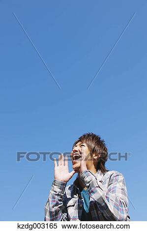 Stock Photography - Young man shouting against blue sky. Fotosearch