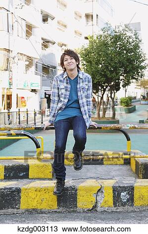 Young man sitting on a guard pipe View Large Photo Image Stock Image - Young man sitting on a guard pipe. Fotosearch