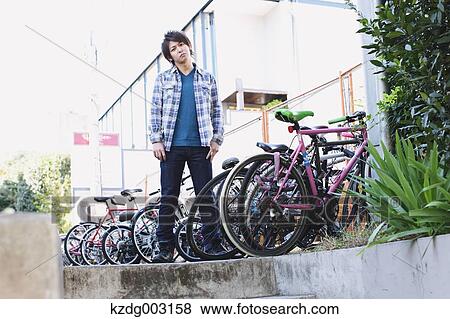 Young man standing by a group of parked bicycles View Large Photo Image Stock Photo - Young man standing by a group of parked bicycles. Fotosearch