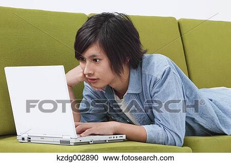 Young man with laptop on the sofa View Large Photo Image Stock Image - Young man with laptop on the sofa. Fotosearch