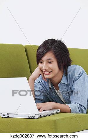 Stock Photo - Young man with laptop on the sofa. Fotosearch
