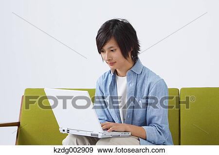Stock Photo - Young man with laptop on the sofa. Fotosearch