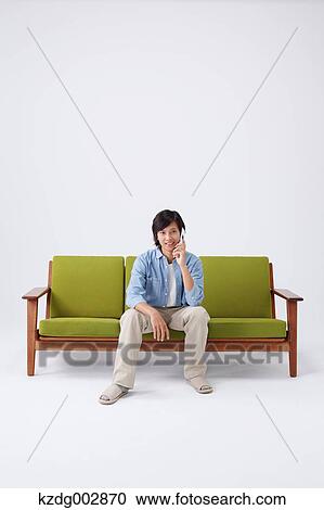 Stock Image - Young man with phone on the sofa. Fotosearch