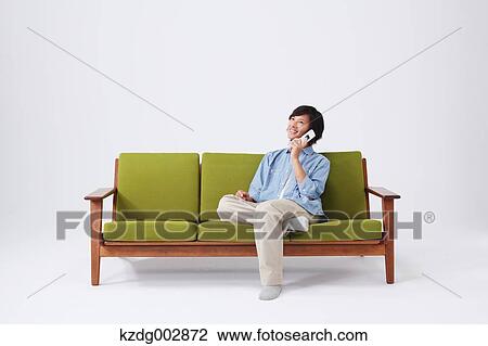 Stock Image - Young man with phone on the sofa. Fotosearch