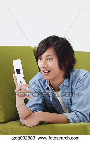 Stock Image - Young man with phone on the sofa. Fotosearch
