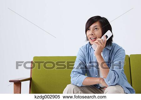 Stock Photography - Young man with phone on the sofa. Fotosearch