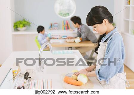 Young mother cooking in an open kitchen with father and son doing homework in the background View Large Photo Image Stock Image - Young mother cooking in an open kitchen with father and son doing homework in the background. Fotosearch