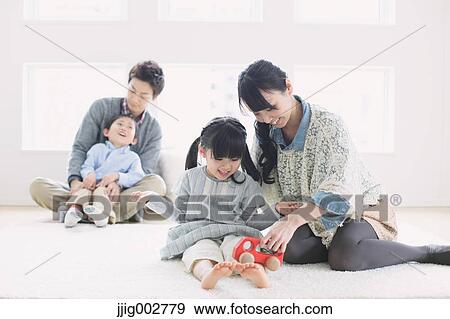 Young mother playing with daughter on the floor. Father and son in the background View Large Photo Image Stock Photo - Young mother playing with daughter on the floor. Father and son in the background. Fotosearch