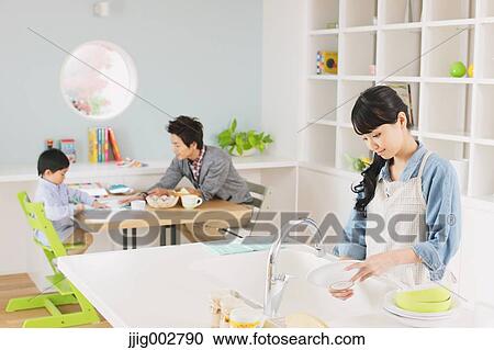 Young mother washing dishes in an open kitchen with father and son doing homework in the background View Large Photo Image Stock Image - Young mother washing dishes in an open kitchen with father and son doing homework in the background. Fotosearch