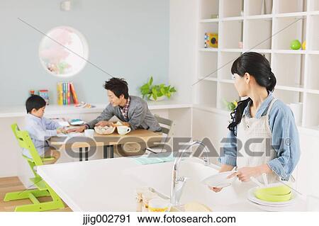 Young mother washing dishes in an open kitchen with father and son doing homework in the background View Large Photo Image Stock Image - Young mother washing dishes in an open kitchen with father and son doing homework in the background. Fotosearch