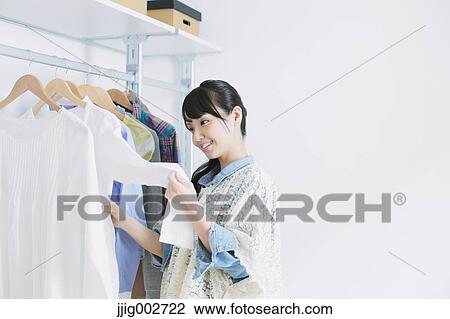 Stock Image - Young woman with long hair choosing clothes in a walk in closet. Fotosearch
