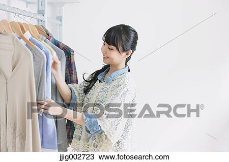 Stock Image - Young woman with long hair choosing clothes in a walk in closet. Fotosearch