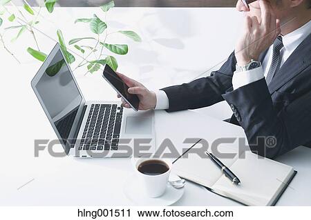 Stock Image - Japanese businessman working with large display smartphone. Fotosearch