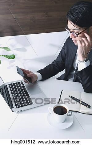Stock Image - Japanese businessman working with large display smartphone. Fotosearch