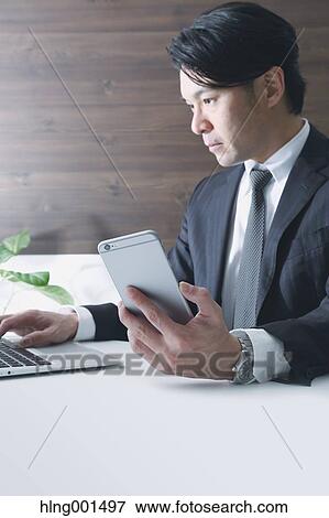 Stock Photo - Japanese businessman working with large display smartphone. Fotosearch