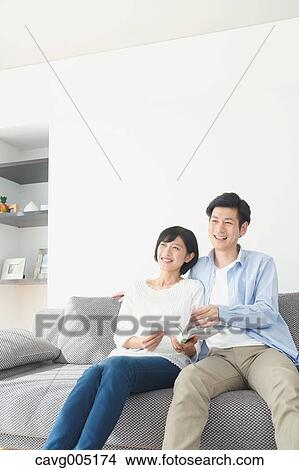 Picture - Japanese couple on the sofa with book. Fotosearch