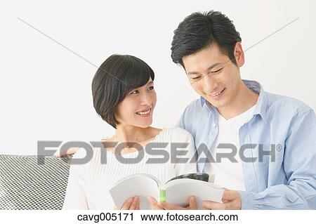 Stock Image - Japanese couple on the sofa with book. Fotosearch