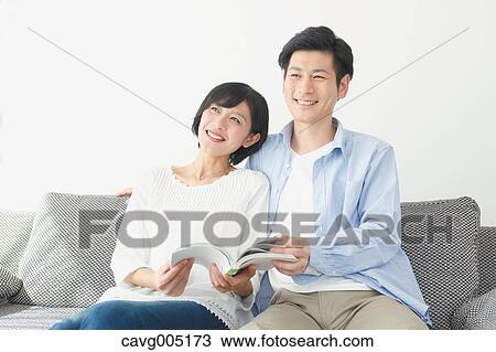 Stock Image - Japanese couple on the sofa with book. Fotosearch
