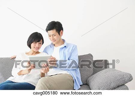 Stock Image - Japanese couple on the sofa with tablet. Fotosearch