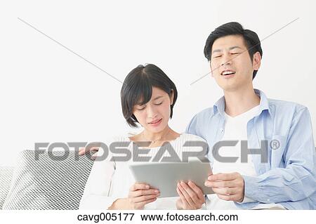 Stock Photo - Japanese couple on the sofa with tablet. Fotosearch